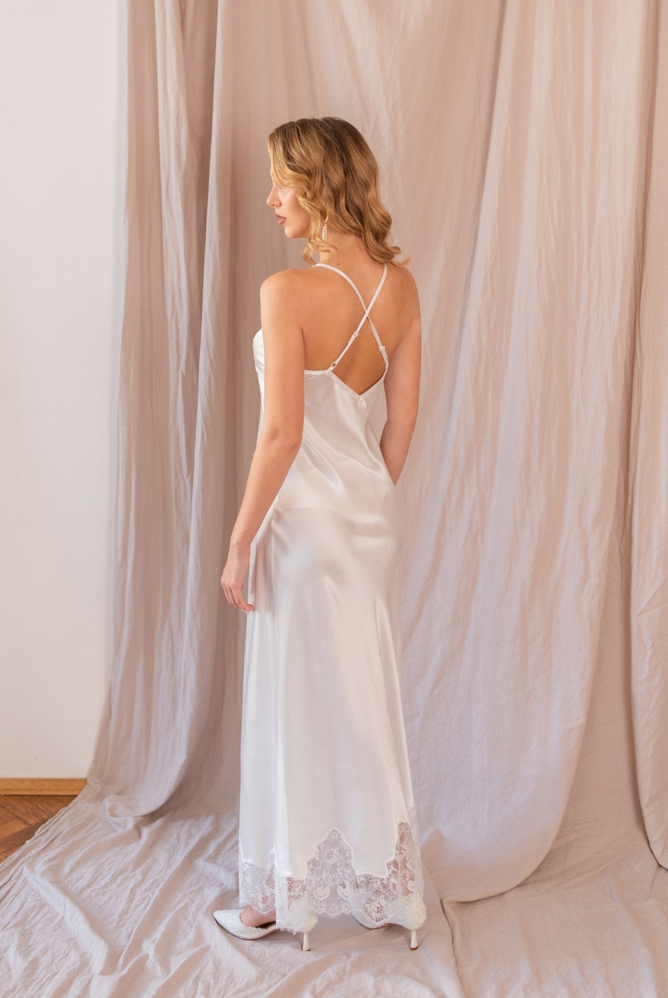Woman in white nightgown with open back, standing in profile against soft beige backdrop