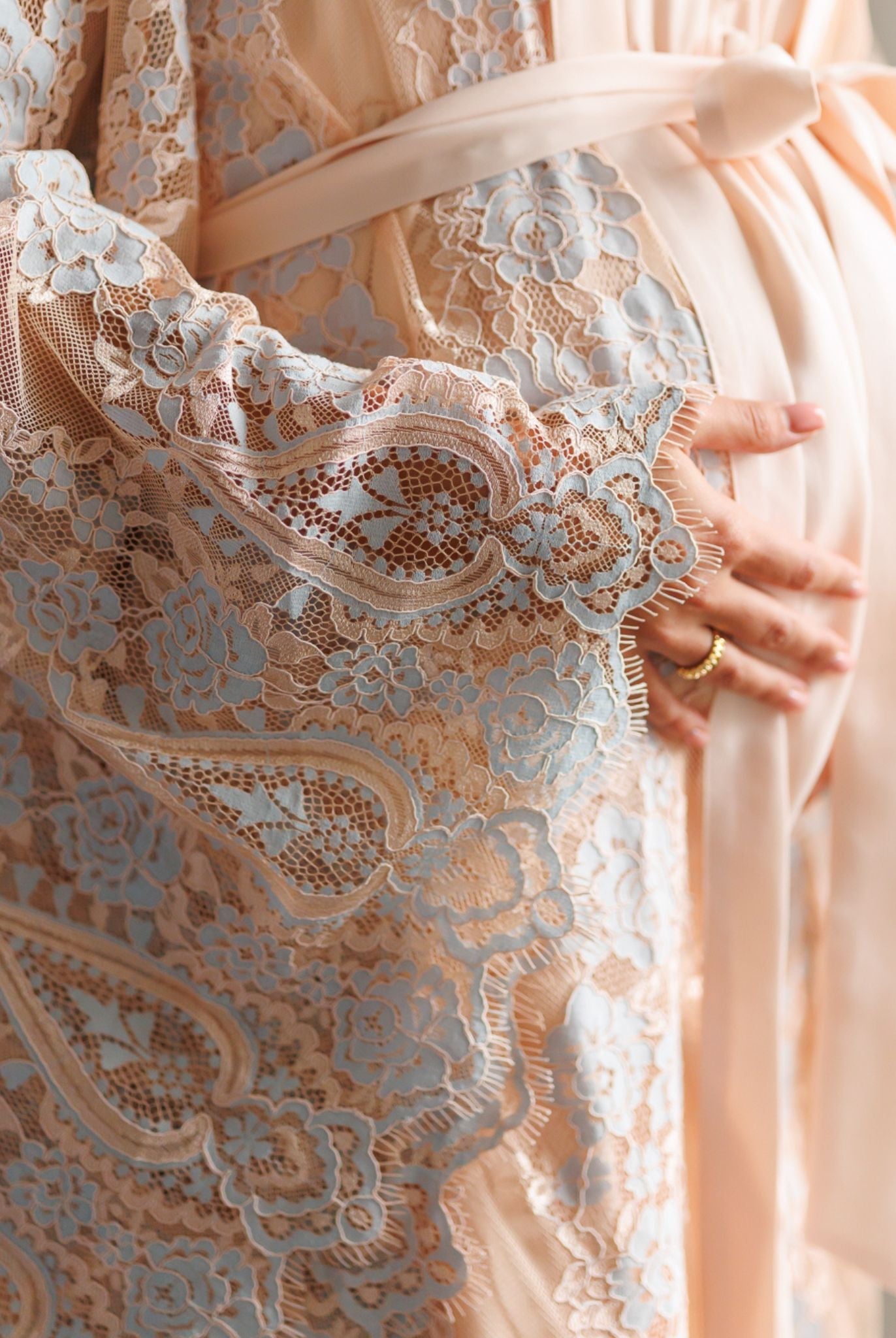 Close-up of intricate lace sleeves and hands on a pregnancy belly, capturing the feminine romance of the fabric.