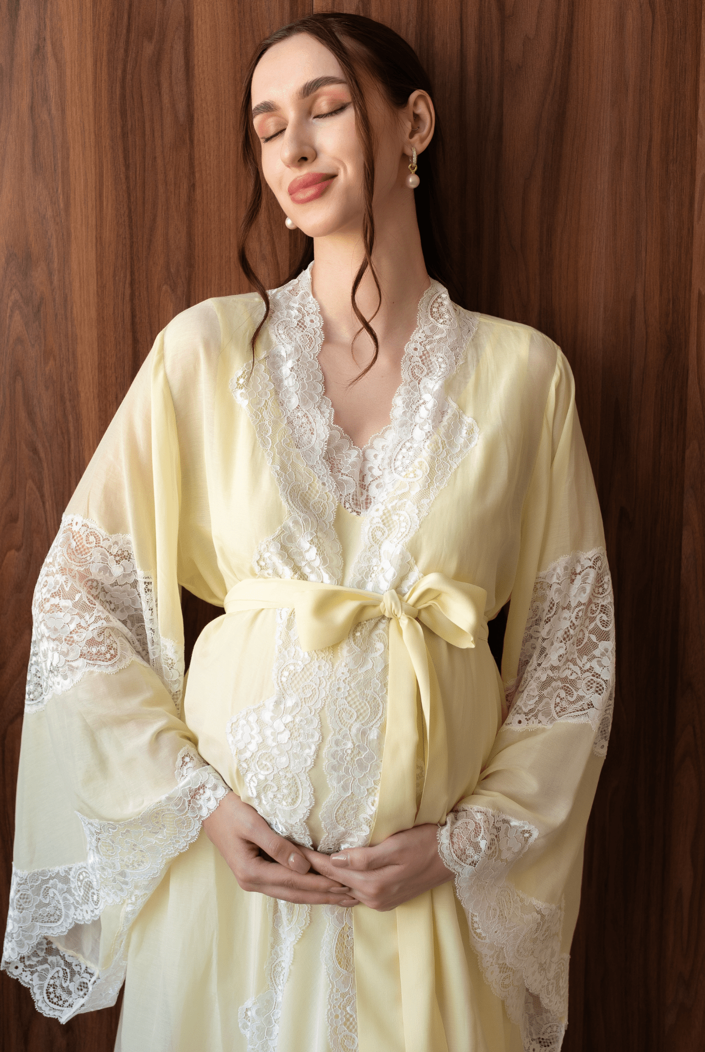 Tender maternity shot in a yellow cotton robe with a sash tied over the baby bump, highlighting soft lace details.
