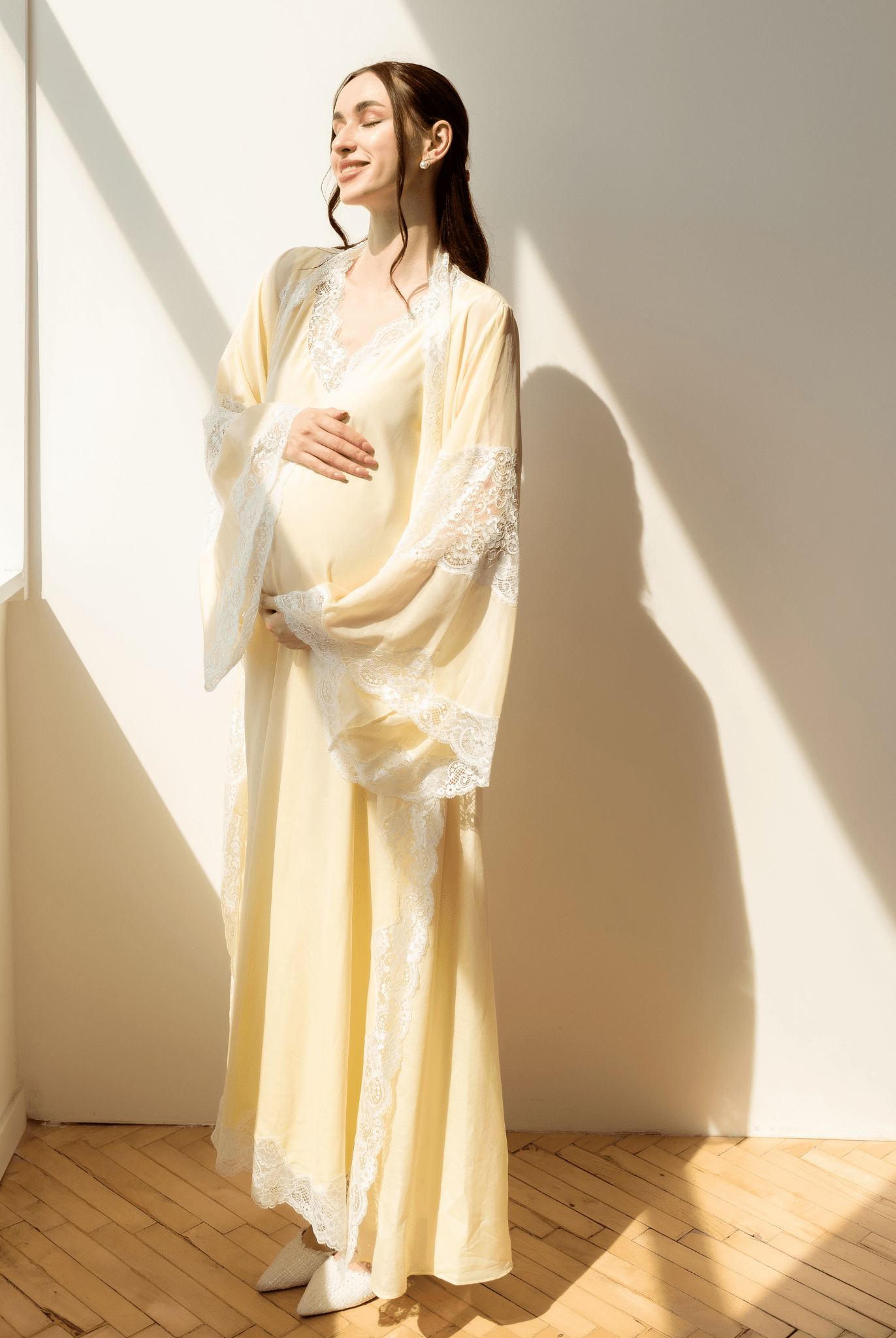 Serene portrait in sunlight, holding a baby bump in a long yellow gown for a tender and graceful maternity look.