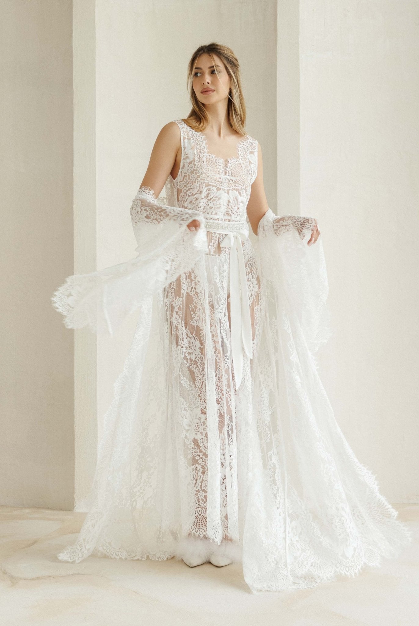 A flowing Bridal Robe draped at the elbows, showcasing the long train and striking lace patterns in motion.
