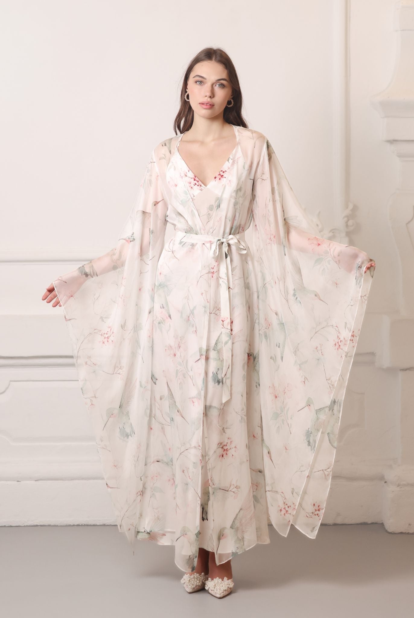 Frontal pose showcasing wide flowing sleeves of a silk chiffon wrap, decorated with romantic floral blooms.