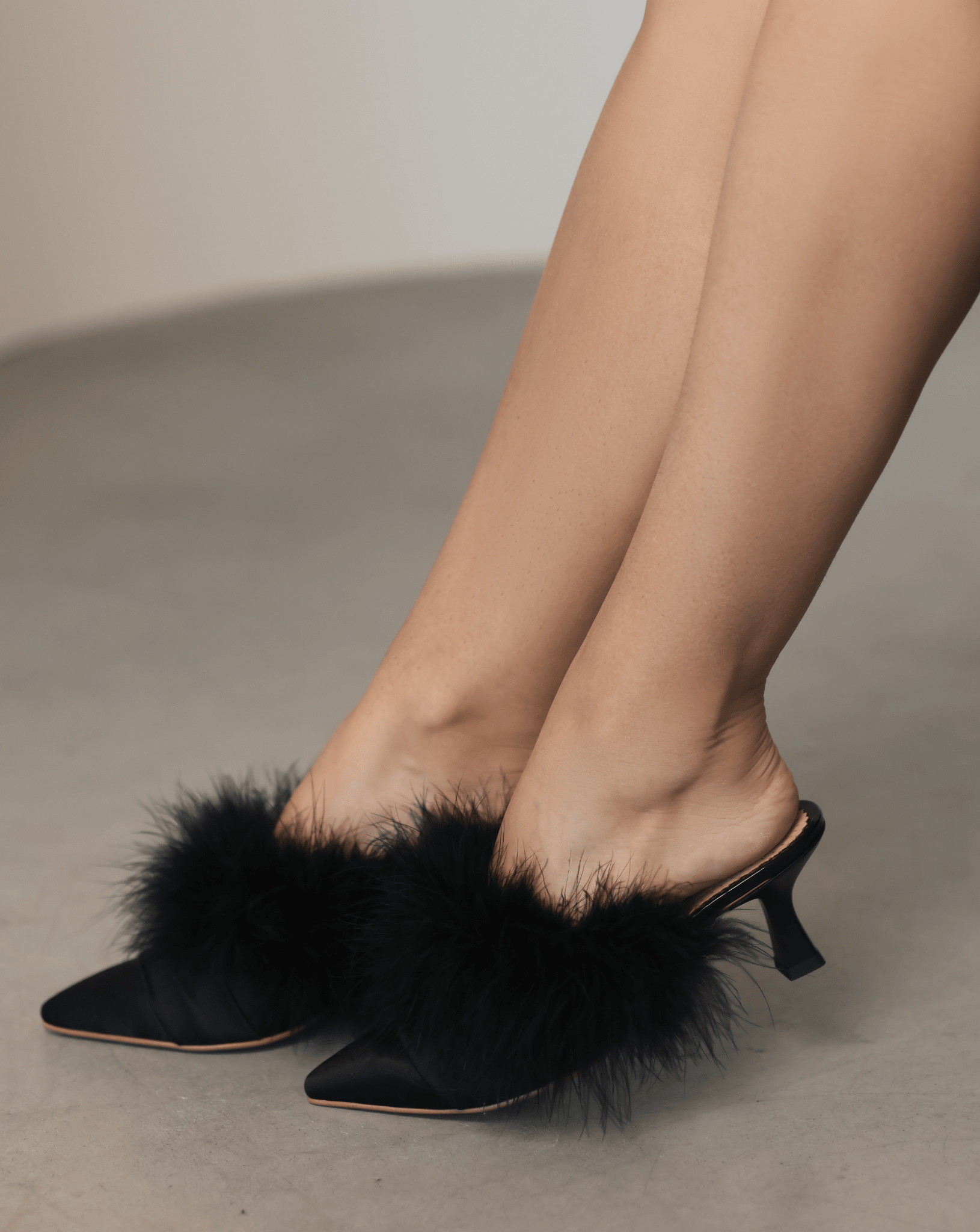 A mid-length shot of the Satin Slippers on the feet, highlighting the pointed-toe form and delicate feathers.