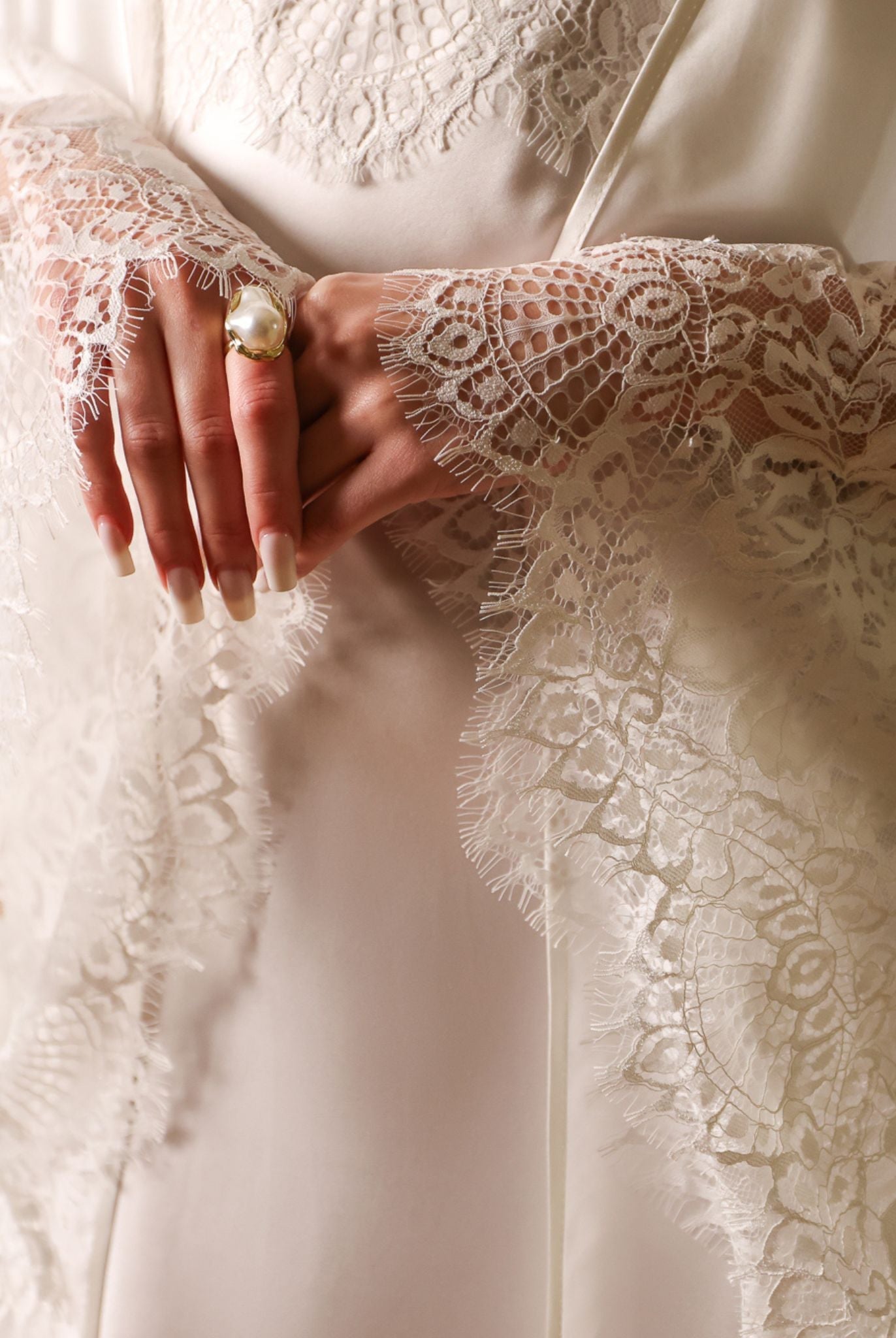 Detailed shot of the hands, focusing on the luxurious lace trimming the wide sleeves of the silk habotai robe.