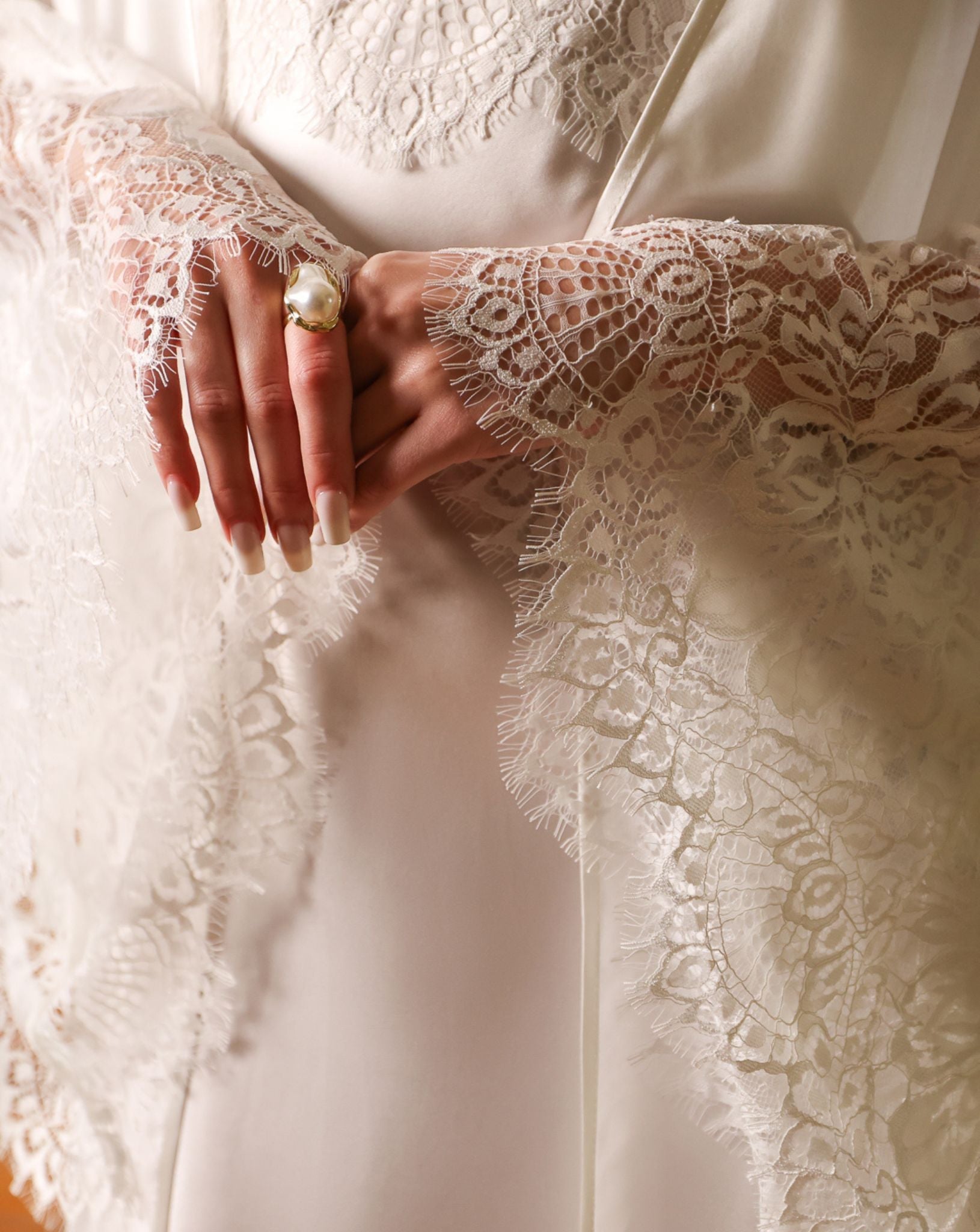 Detailed shot of the hands, focusing on the luxurious lace trimming the wide sleeves of the silk habotai robe.
