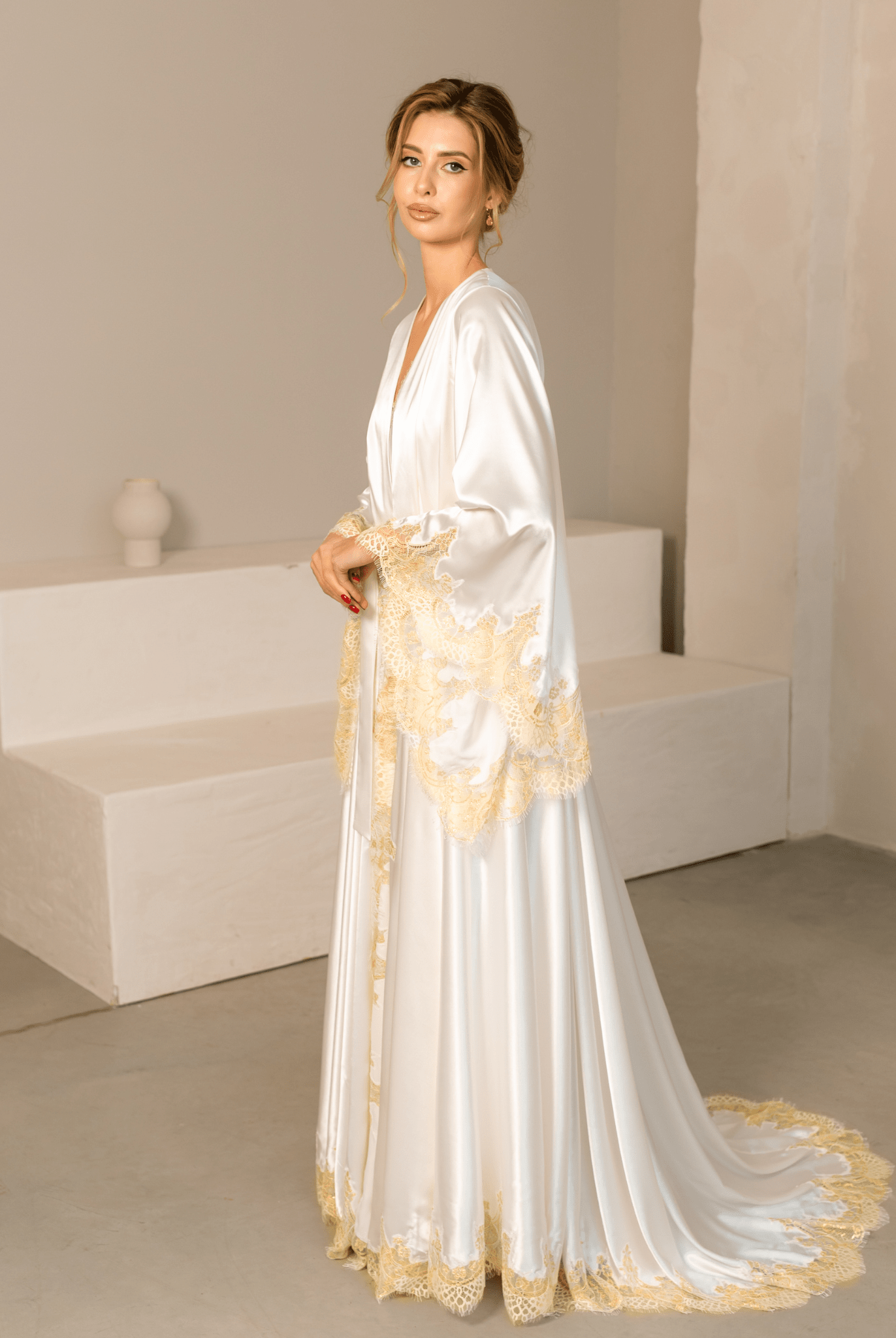 Side view of a white satin robe with a long flowing train and decorative gold lace along the edges.