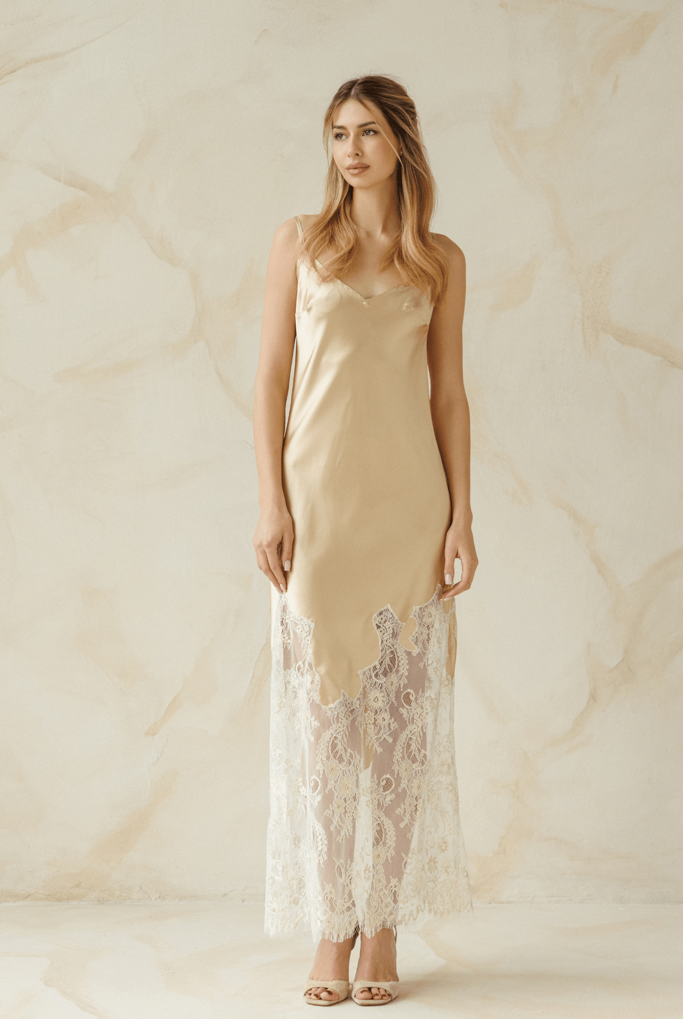 Model in beige satin nightgown with lace hem, standing in natural light