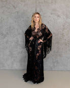 Bride in white lace robe with long train, standing in front of wooden backdrop – KÂfemme
