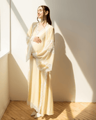 Serene portrait in sunlight, holding a baby bump in a long yellow gown for a tender and graceful maternity look.