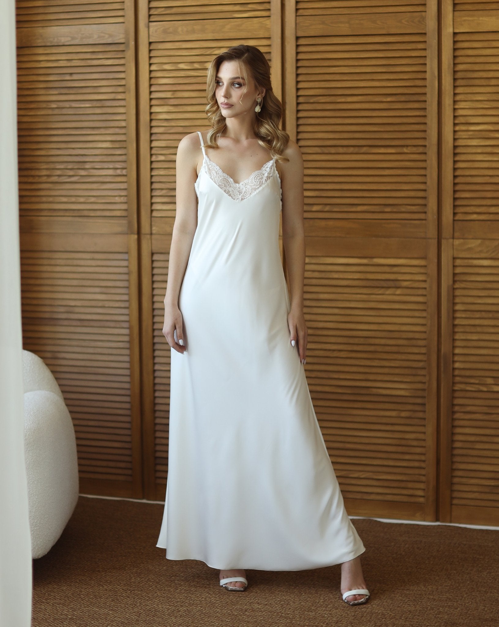 Bride in flowing white robe and nightgown, standing near wood panel