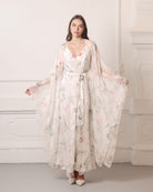 Frontal pose showcasing wide flowing sleeves of a silk chiffon wrap, decorated with romantic floral blooms.