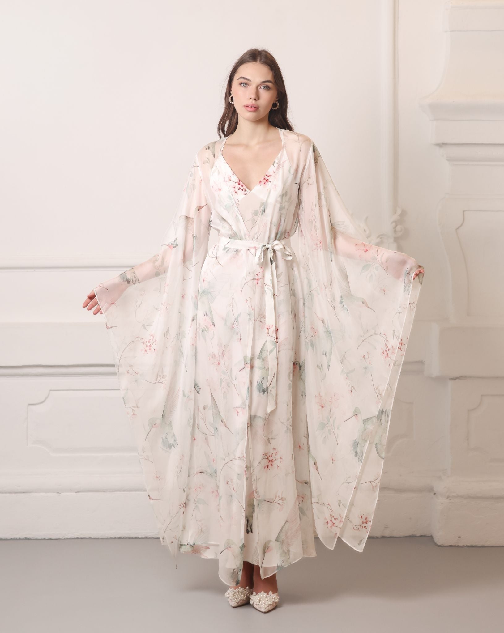 Frontal pose showcasing wide flowing sleeves of a silk chiffon wrap, decorated with romantic floral blooms.