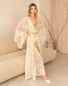 Woman wearing sheer lace robe and nightgown set in soft blush, standing in a minimal beige interior - Kafemme Loungewear