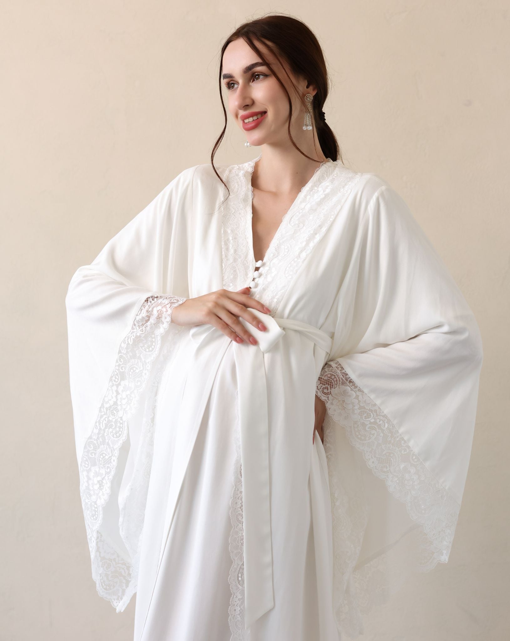 Posing with a hand on the belly to display the wide sleeves finished with fine lace for a sophisticated look.