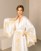 Close-up of a white satin robe featuring gold lace accents on the top and voluminous wide sleeves.