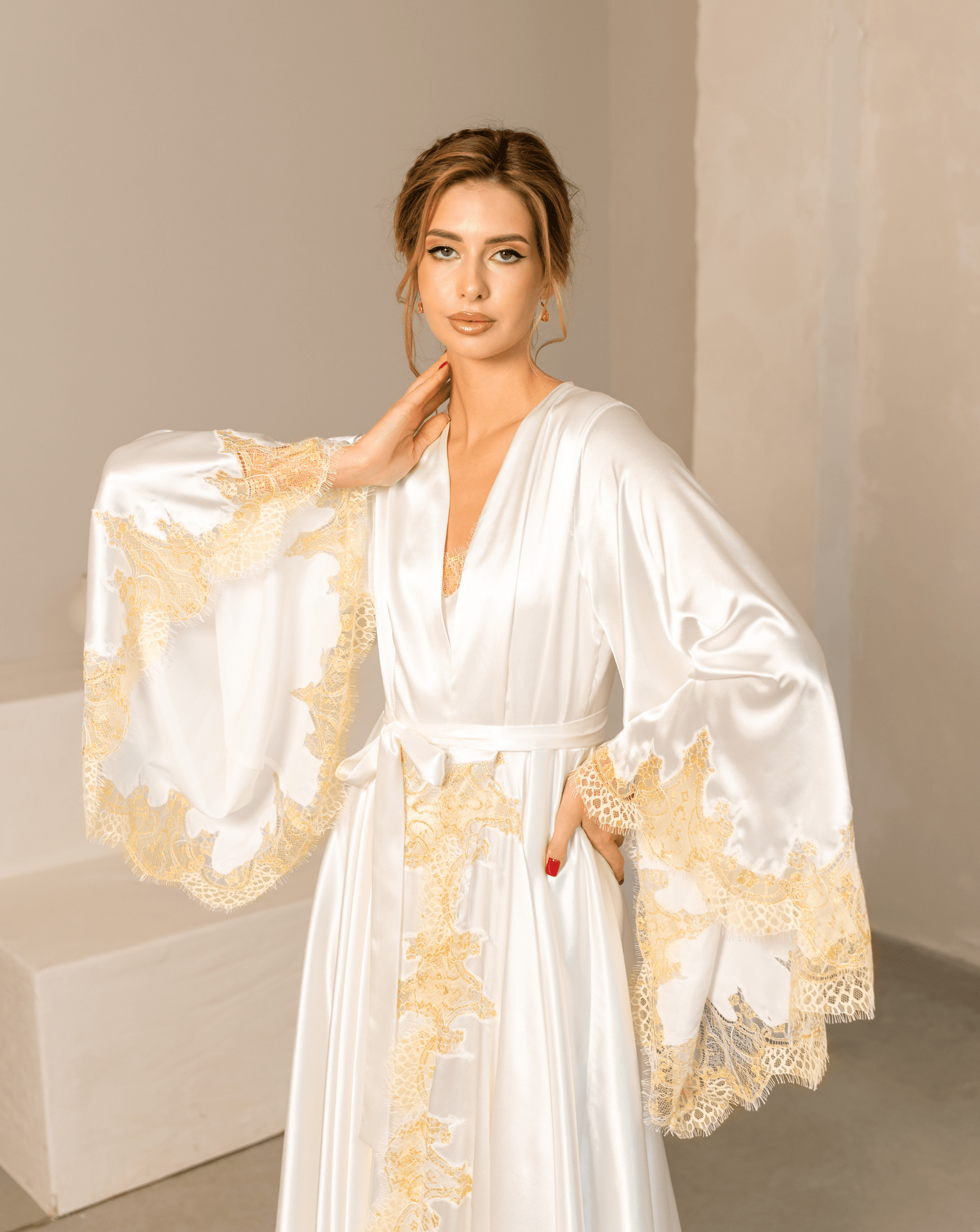 Close-up of a white satin robe featuring gold lace accents on the top and voluminous wide sleeves.