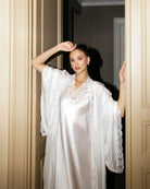 Artistic waist-up shot between doors, capturing the soft luminous sheen of the bridal silk garment and lace details.